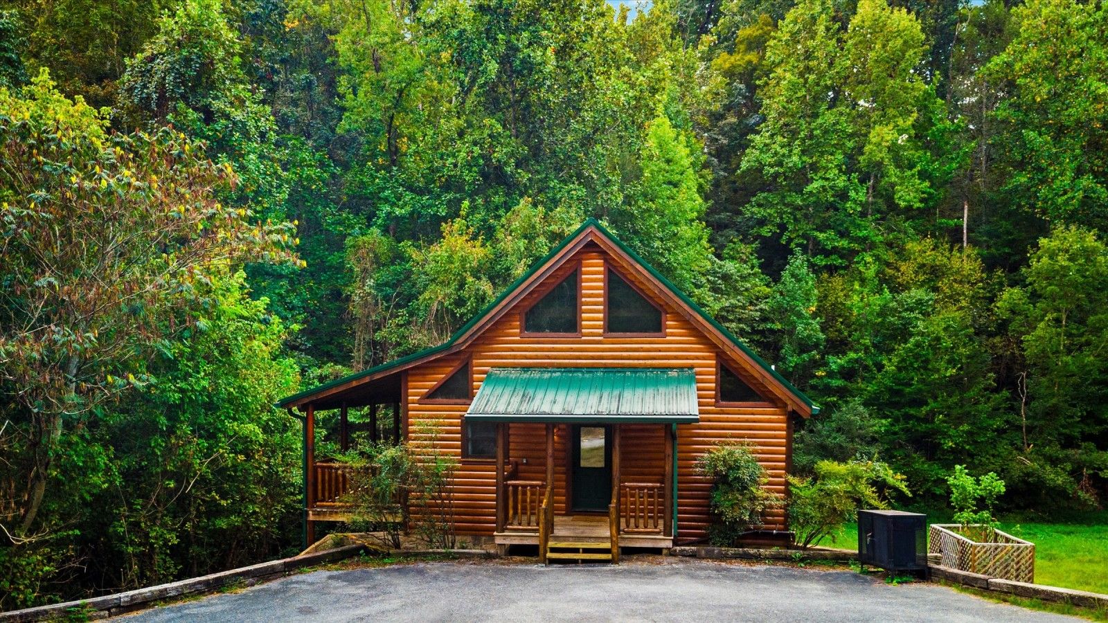 Une cabane en rondins dotée d’un porche, entourée d’une forêt dense.