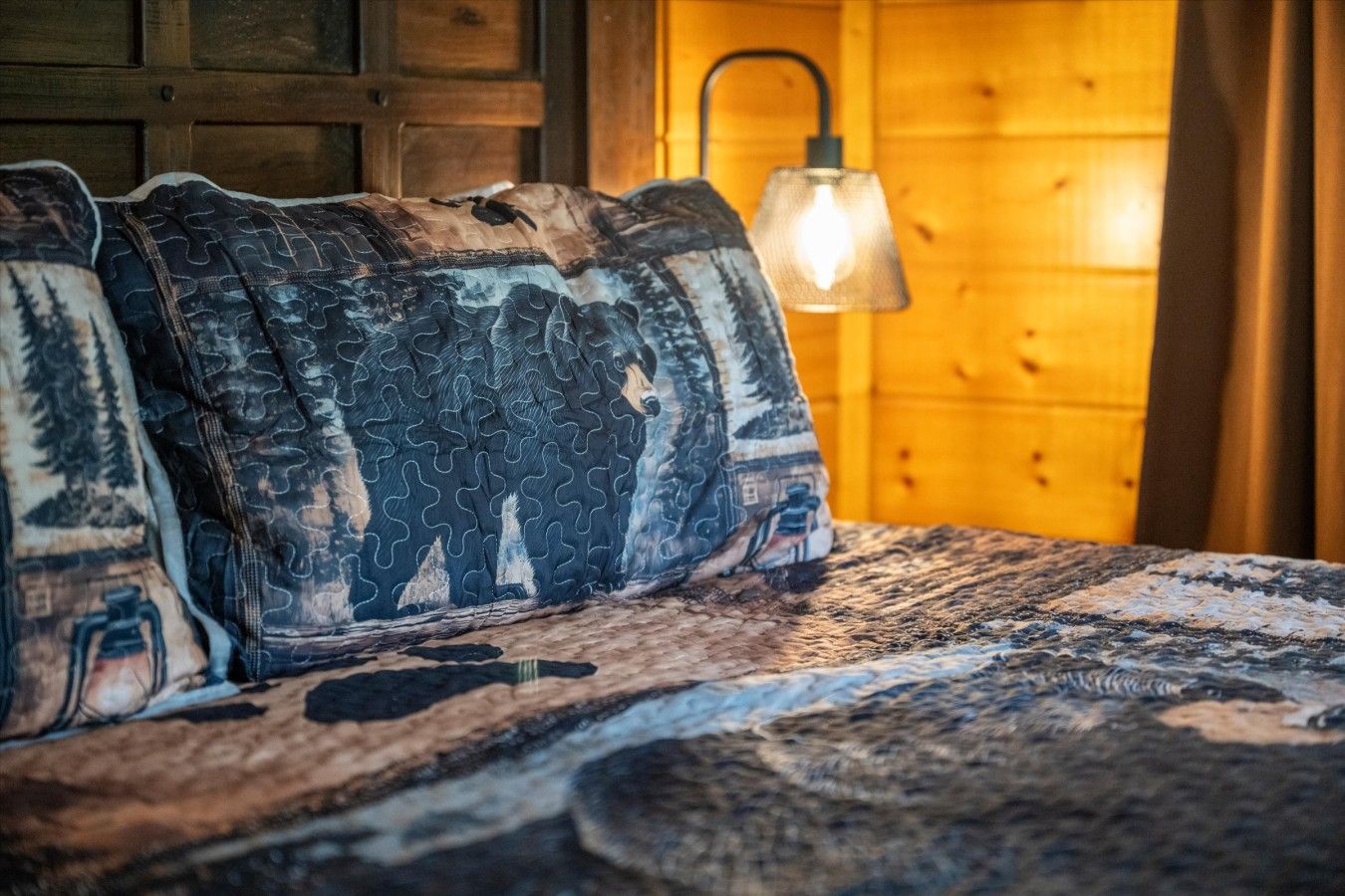 A bed with patterned bedding and a wall-mounted lamp.