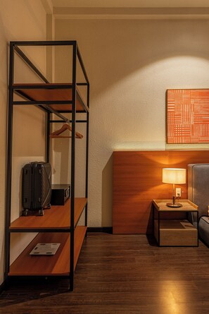 A hotel room with a wooden floor, a metal shelf unit, a lamp on a side table, and a wall-mounted artwork. - The Cozy Hideout: Studio Inside a Charming Cafe (Cau Ong Lanh)