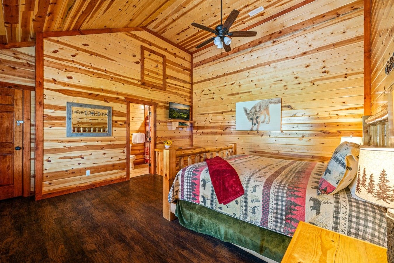 Interior de cabana de madeira com cama, ventilador de teto e pintura de uma raposa.