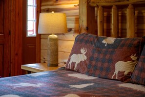A bed with a patterned bedspread and two pillows with moose designs, a lamp, and wooden walls. - 6BR Pool Cabin w/Hot Tub*Theater*MTN Views*Games (Sevierville)