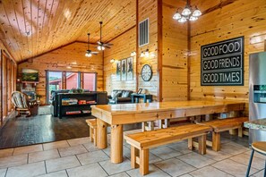 Un intérieur en bois comprenant un coin repas, une cheminée et une enseigne sur laquelle on peut lire : « BONNE NOUVELLE, BONS AMIS, BONS MOMENTS ».