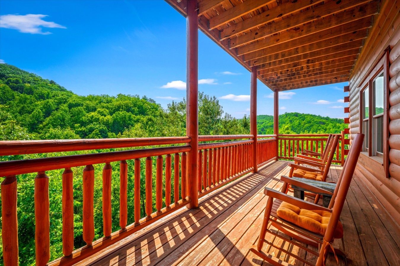 A wooden deck with a railing, wooden chairs, and a view of a forested hillside.