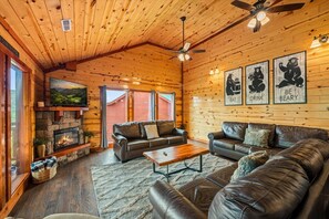 Un intérieur de chalet chaleureux avec une cheminée, des canapés en cuir et un ventilateur de plafond.