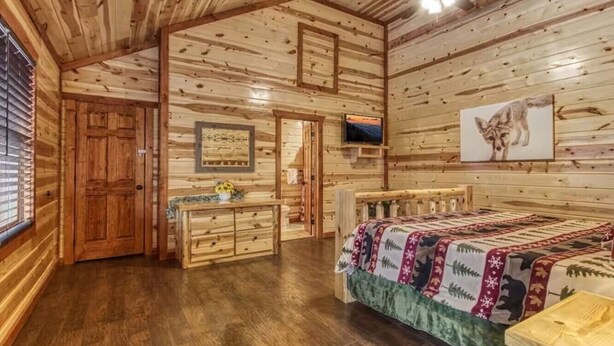 Ein Schlafzimmer in einer Blockhütte mit einem Bett, einem Schminktisch und einem Fernseher an der Wand.