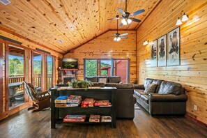 A cozy cabin interior with a fireplace, leather sofas, a coffee table with board games, and a TV mounted on the wall. - 6BR Pool Cabin w/Hot Tub*Theater*MTN Views*Games (Sevierville)