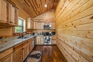 A wooden cabin interior with a kitchen featuring a microwave, oven, and sink. - New! 3BR w/Hot Tub*Game Room*Comm Pools*Fireplace (Gatlinburg)