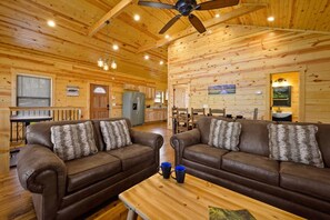 A cabin interior with two leather sofas, a wooden dining table, and a ceiling fan. - New! 3BR w/Hot Tub*Game Room*Comm Pools*Fireplace (Gatlinburg)