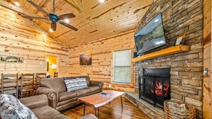 Ein gemütliches Blockhaus-Interieur mit Kamin aus Stein, Holzwänden, einer Ledersofa und einem Deckenventilator.