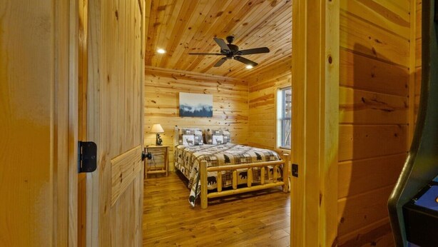 Ein Schlafzimmer einer Holzhütte mit einem Bett, einem Deckenventilator und einem Fenster.