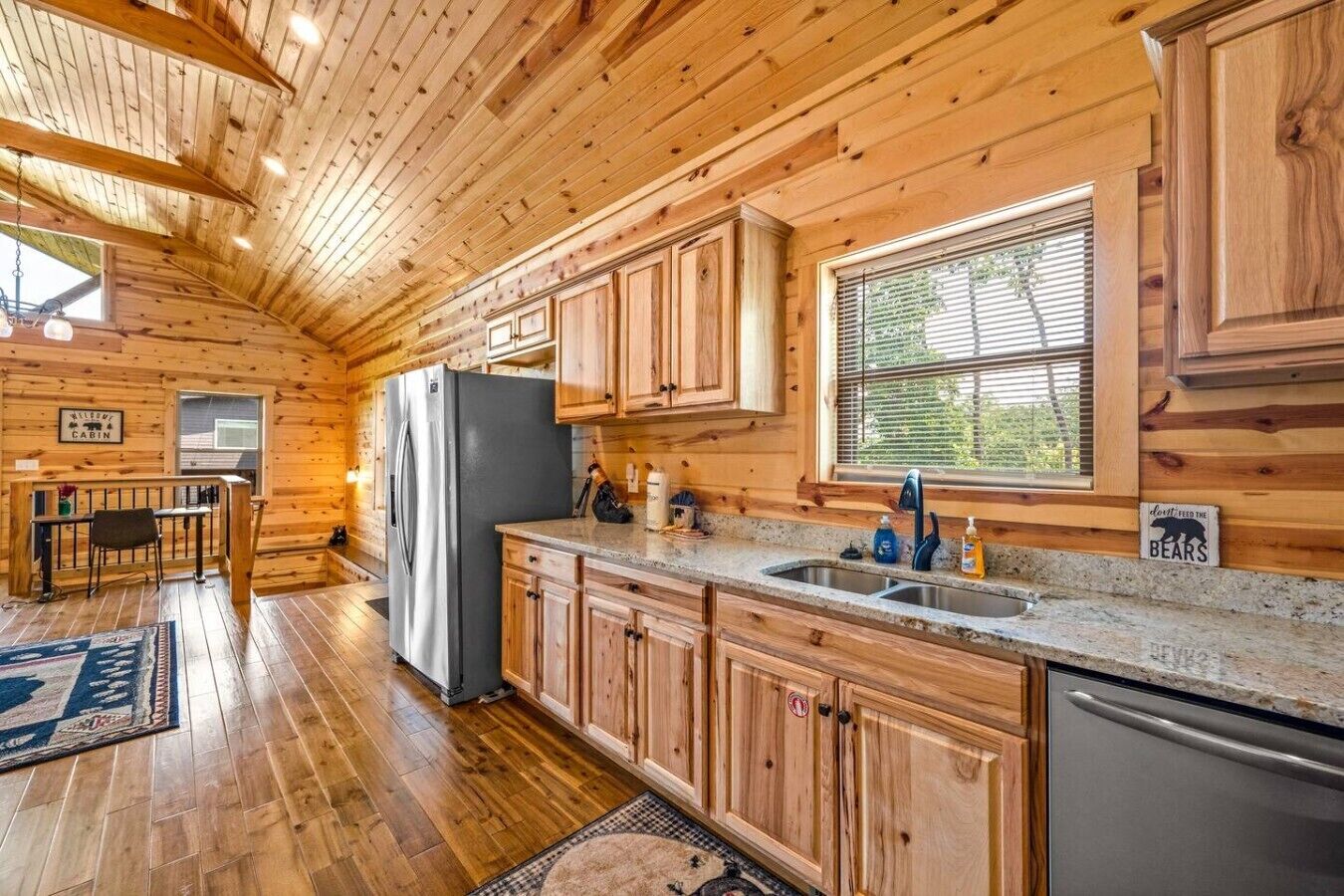 Ein Ferienhäuschen mit Holzwänden, einer Küche inklusive Kühlschrank, Spüle und Schränken, sowie einem Essbereich mit Tisch und Stühlen.