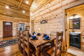 Un interior de madera con una mesa de comedor para cuatro, paredes de madera y una zona de cocina con un lavamanos y armarios.