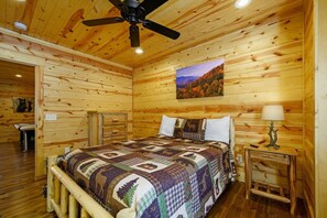 Ein Schlafzimmer einer Holzhütte mit einem Bett, einem Deckenventilator, einem Gemälde und einem Nachttisch mit Lampe.