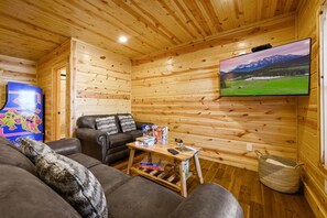 A cozy cabin interior with a wooden interior, a sofa, a coffee table, and a television mounted on the wall. - New! 3BR w/Hot Tub*Game Room*Comm Pools*Fireplace (Gatlinburg)
