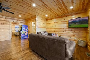 Ein Holzinterieur mit einer Couch, einem an der Wand montierten Fernseher und einem Deckenventilator.