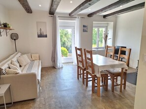 A room with a dining table and chairs, a sofa, a bed, and a view of greenery outside. - Cosy cottage • Baie du Mont‑Saint‑Michel • Entre terre, baie & mer (Sougeal)