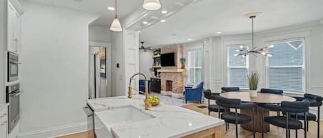 A modern kitchen with a central island, a dining area with round tables and chairs, and a fireplace.
