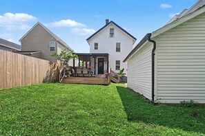 Un jardin à l’arrière d’une maison, avec une terrasse en bois, un porche à l’avant et une maison à deux étages.
