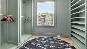 A walk-in closet with open shelving, a window with a view of buildings, and a patterned rug on the floor. - Luxurious curated high end oasis (Cincinnati)