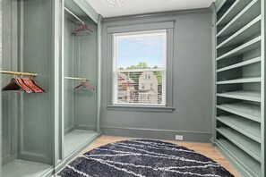 Um closet espaçoso com prateleiras abertas, uma janela com vista para prédios e um tapete estampado no chão.