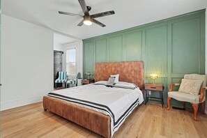 Quarto com cama, uma cadeira, mesa de cabeceira, abajur e ventilador de teto.