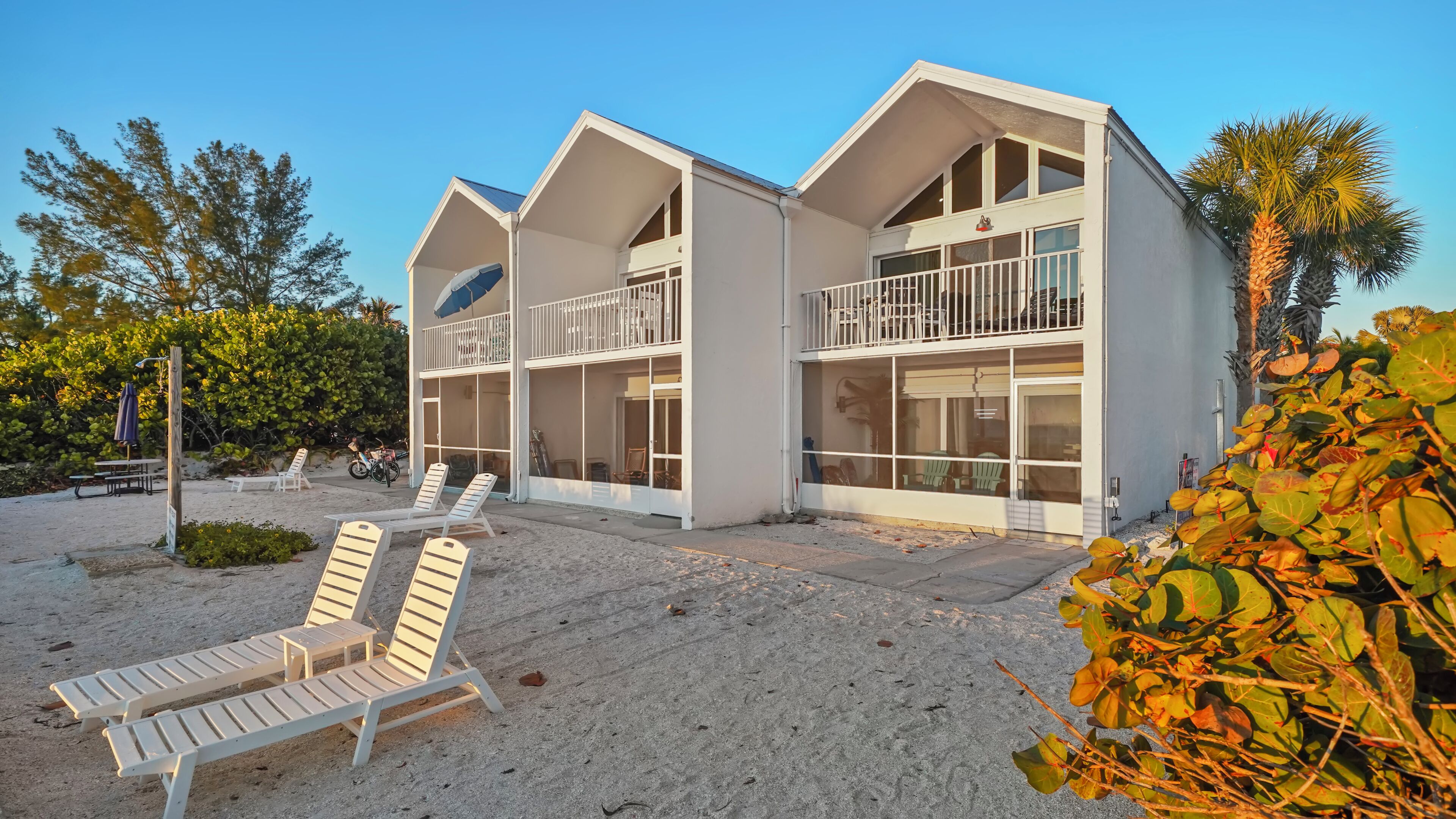 A beachfront property with a two-story building, outdoor seating, and a sandy beach area.