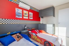 Quarto com cama de carro de corrida, parede quadriculada e travesseiro com carro de corrida.