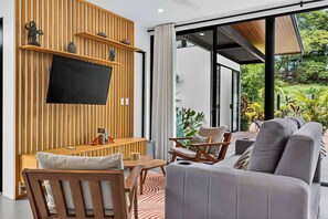 A modern living room with a flat-screen TV mounted on a wooden wall, a sofa, a wooden coffee table, and a chair. - Modern Villa, Pool, Nature & Beach (Matapalo, Cabo Velas)