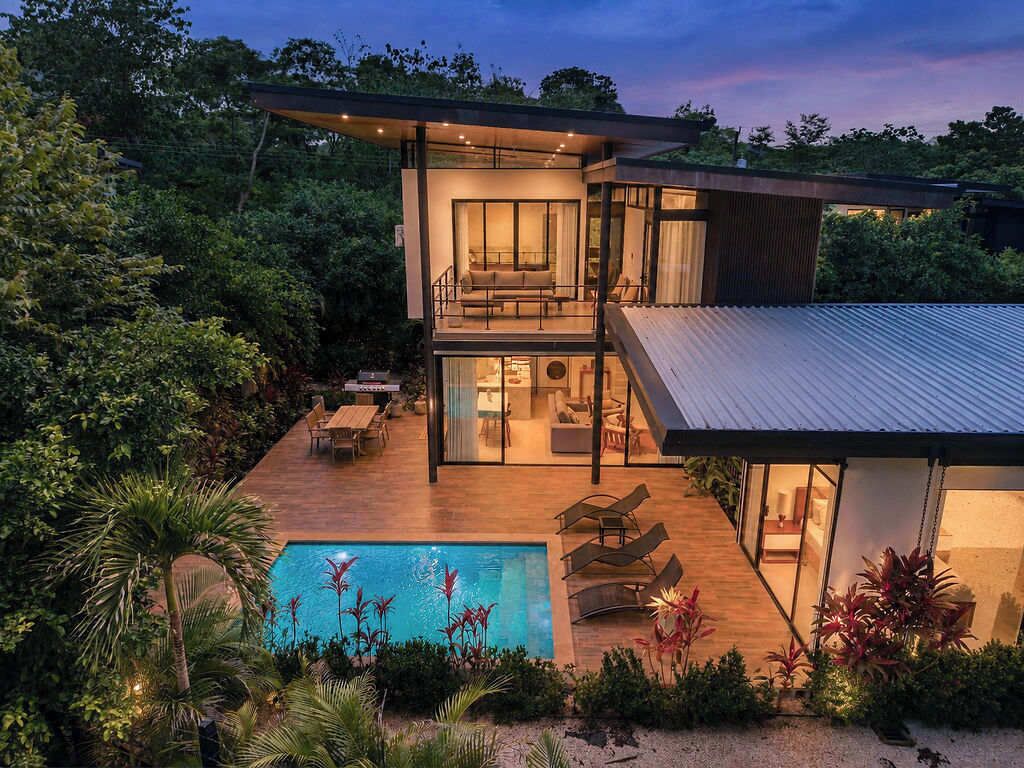 Ein modernes, zweistöckiges Haus mit Pool, Sitzgelegenheiten im Freien und üppiger Bepflanzung.