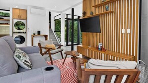 Una sala moderna con un sofá gris, detalles de madera, un televisor de pantalla plana y una escalera que lleva a un balcón.