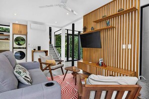 A modern living room with a grey sofa, wooden accents, a flat-screen TV, and a staircase leading to a balcony. - Modern Villa, Pool, Nature & Beach (Matapalo, Cabo Velas)