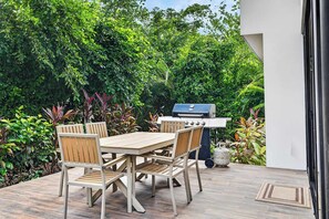 An outdoor patio with a wooden table and chairs, a barbecue grill, and lush greenery. - Modern Villa, Pool, Nature & Beach (Matapalo, Cabo Velas)