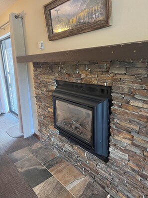 A stone fireplace with a modern design, a framed picture above it, and a door leading to a hallway. - Walk Out Ski In 2 Bed 2 Bath (Crested Butte)