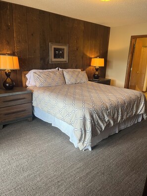 A bedroom with a bed, two bedside tables, a nightstand, a wooden headboard, a framed picture, and a door. - Walk Out Ski In 2 Bed 2 Bath (Crested Butte)