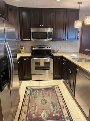 A modern kitchen with dark wood cabinets, stainless steel appliances, and a decorative fish-patterned rug. - Walk Out Ski In 2 Bed 2 Bath (Crested Butte)