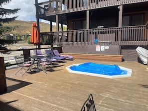 Una terraza de madera con piscina, sillas de descanso y una mesa.