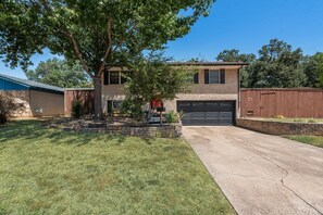 A two-story house with a garage, a tree in the front yard, and a well-maintained lawn. - I129 - 3BD Pool Retreat | Fire Pit & Backyard | Irving (Irving)