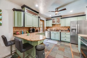 A kitchen with green cabinets, a granite countertop, a stainless steel refrigerator, and a ceiling fan. - I129 - 3BD Pool Retreat | Fire Pit & Backyard | Irving (Irving)