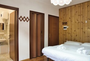 Une chambre d’hôtel avec un lit, un mur recouvert de panneaux en bois, une porte et une salle de bain visible à travers une porte ouverte.