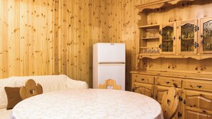 Una habitación con paredes de madera, una cama con colcha estampada, un refrigerador blanco y armarios de madera con puertas de cristal.