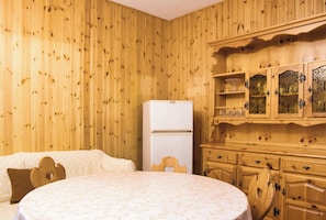 Een kamer met houten wanden, een bed met een bloemenprint beddegoed, een witte koelkast en houten kastjes met glazen deuren.