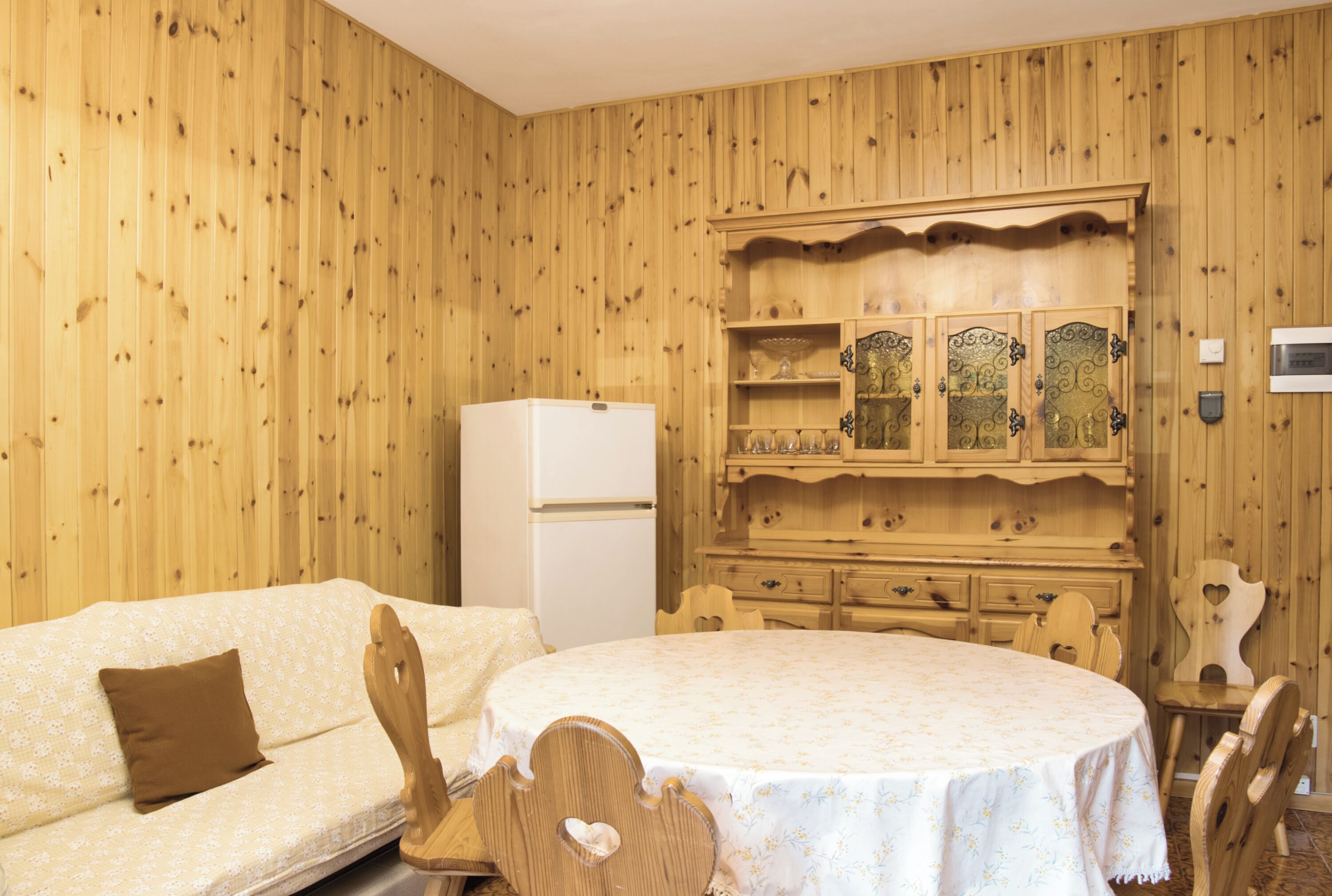 Ein Zimmer mit Holzwänden, einem Bett, einem Tisch und einem Schrank mit Glastüren.