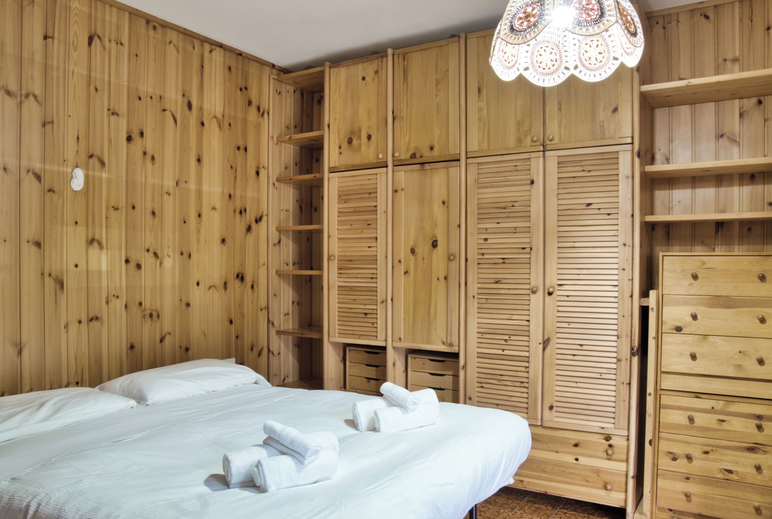 Ein Zimmer mit Holzwänden, einem Bett mit weißer Bettwäsche und einem Kleiderschrank mit mehreren Fächern.