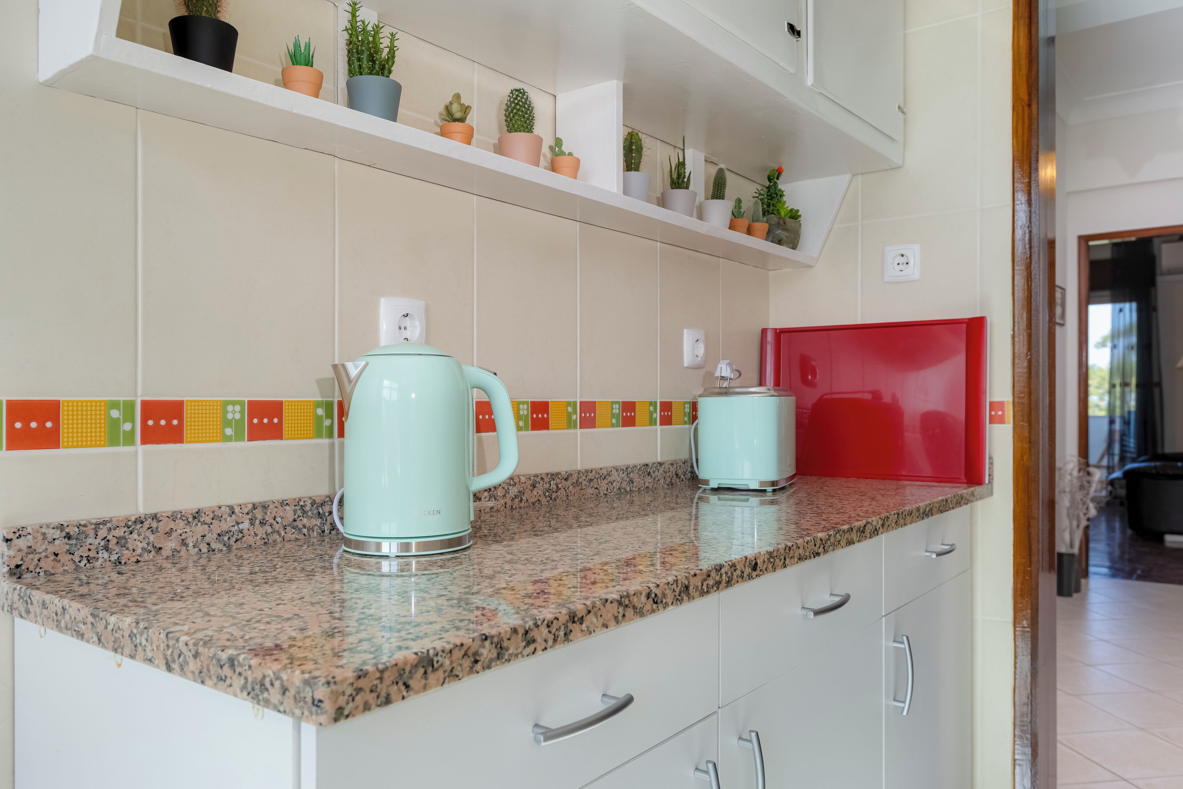 A kitchen with granite countertops, a red microwave, and a variety of potted plants on a shelf.