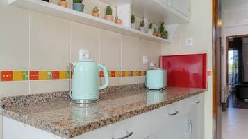 A kitchen with granite countertops, a red microwave, and a variety of potted plants on a shelf.