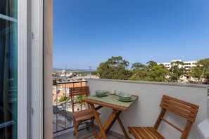 A balcony with a table and chairs, overlooking a coastal area with buildings and trees. - Brise Marine Apartment - D. Ana Beach (Lagos)