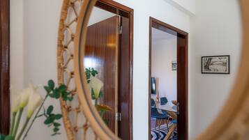 A room with a wooden door, a framed picture on the wall, and a mirror reflecting a dining area with chairs and a table.