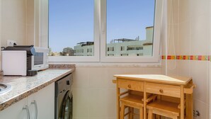 A compact kitchen with a washing machine, a microwave, and a wooden table. - Sea Breeze Apartment - D. Ana Beach (Lagos)