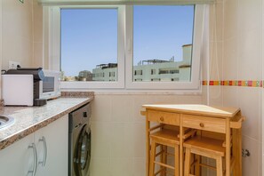 Eine kompakte Küche mit Waschmaschine, Mikrowelle und einem Holztisch.