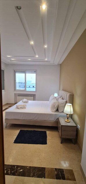 Hotelkamer met een bed, nachtkastje, lamp, raam en uitzicht over de stad.